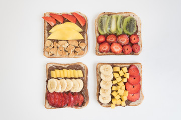 There are four sandwiches on the white surface. Bread covered with chocolate paste, strawberry and banana, mango. A sweet Breakfast.