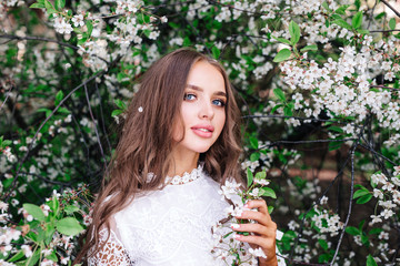 Portrait of a beautiful young woman in white dress in flowering spring