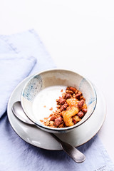 Healthy breakfast yogurt bowl with granola and caramelized bananas and nuts on grey concrete background. Selective focus