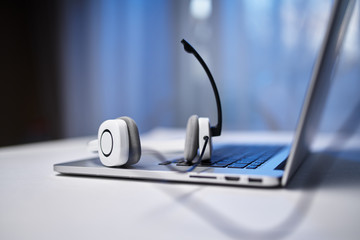 Obraz na płótnie Canvas Laptop, white headphones with microphone on blurry blue background.