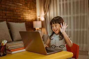 little kid video calling using laptop at home in the evening with school teacher