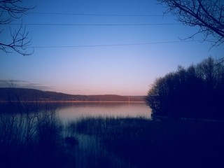 frozen lake in winter season close to the village with forest reflecting in water