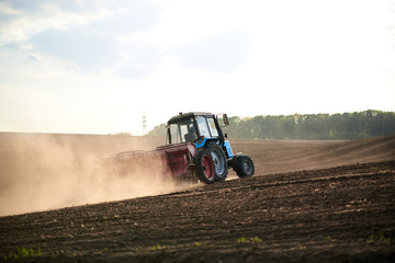 Agricultural work on field with black soil. Blue tractor riding and seeding countryside. Rural works in spring. Environmental protection concept. Ecological products cultivation. Natural background.