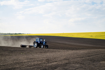 Agricultural work on field with black soil. Blue tractor riding and seeding countryside. Rural works in spring. Environmental protection concept. Ecological products cultivation. Natural background.