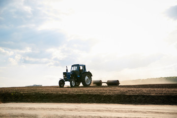 Obraz premium Agricultural work on field with black soil. Blue tractor riding and seeding countryside. Rural works in spring. Environmental protection concept. Ecological products cultivation. Natural background.