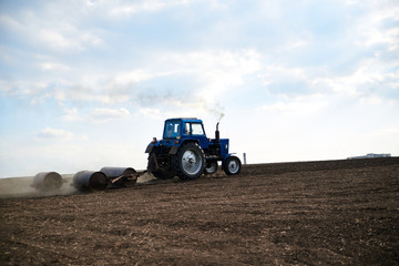 Agricultural work on field with black soil. Blue tractor riding and seeding countryside. Rural works in spring. Environmental protection concept. Ecological products cultivation. Natural background.