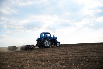 Agricultural work on field with black soil. Blue tractor riding and seeding countryside. Rural works in spring. Environmental protection concept. Ecological products cultivation. Natural background.