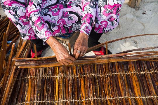 Mani di una vecchia donna alle Maldive impegnate nella tessitura di foglie e rami a costruire tappeti e oggetti d&rsquo;uso comune