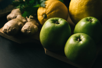 Composition of fruits, still life. Components of Asian cuisine. Lemon with ginger and green apples and herbs on a wooden board and on a dark background