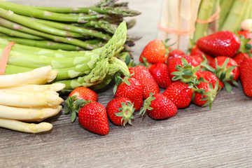 Grüne Spargel, weiße Spargel und frische Erdbeeren dekoriert auf einem rustikalen Holztisch