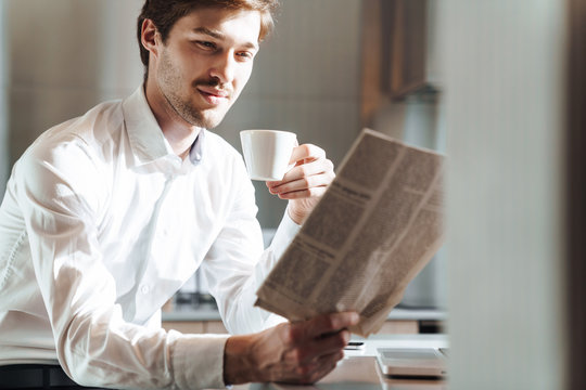 Photo of pleased businessman drinking coffee and reading newspaper