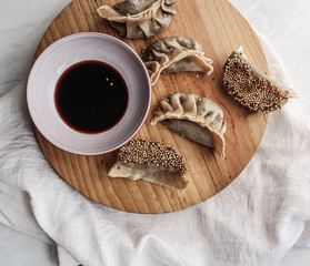Asian dumplings pan fried with soy sauce on a wooden table. Wooden chopsticks on the side. White background. Flat lay with copy space. 