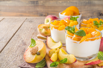 Curd or yogurt dessert with canned and fresh peaches, on wooden rustc background. Summer breakfast fruit dessert.