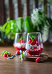 Homemade cottage cheese with fresh raspberries in a glass glass on a rustic wooden background. Dietary breakfast. Russian cottage cheese with berry and mint.