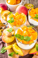 Curd or yogurt dessert with canned and fresh peaches, on wooden rustc background. Summer breakfast fruit dessert.