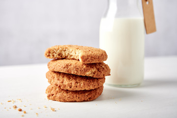 Stack of cookies in front of milk bottle with tag on white wooden table against light grey grunge background, close-up side view