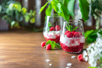 Homemade cottage cheese with fresh raspberries in a glass glass on a rustic wooden background. Dietary breakfast. Russian cottage cheese with berry and mint.