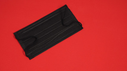 Black Disposable Ear- loop face mask on red background.