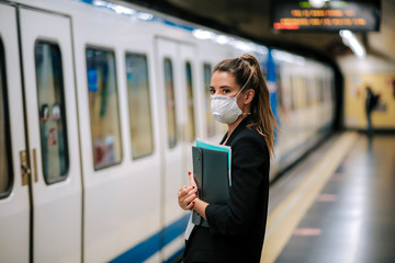 young woman waits for the subway with a medical mask