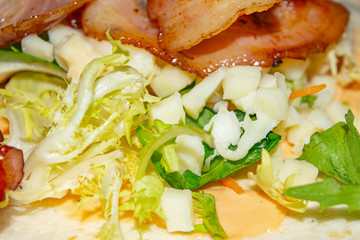 Leafy salad, sliced vegetables, sauce and fried bacon slices on pita bread are the basis for homemade Shawarma. Close up.