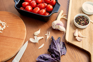 High angle view of container with tomatoes, knife and cutting boards with ingredients on wooden background