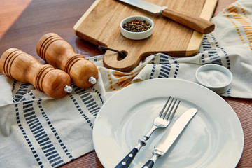 High angle view of plate with cutlery near cloth, cutting board, bowls, pepper and salt mills on...
