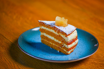 Slice of layered vanilla honey cake served on a blue plate on rustic wooden table over blurred restaurant background.