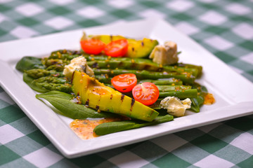 Healthy grilled avocado and asparagus salad with linen seeds and tomatoes. Served on a white square plate.