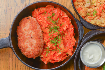 Delicious potato pancakes with sour cream, rice with meat and vegetables and Chicken Kiev cutlet served in frying pans.