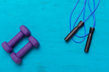 Jumping rope and dumbbells on blue wooden background. Workout online concept.