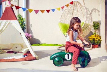 cute young girl, child riding a toy car, playing on summer patio