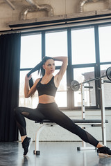 Sportswoman sitting on sport equipment and looking away near barbell in gym