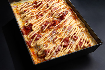 detroit pizza on an iron tray on a dark background. selective focus