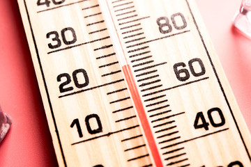 Wood thermometer shows high  temperatures in fahrenheit or celsius on light pink background with...