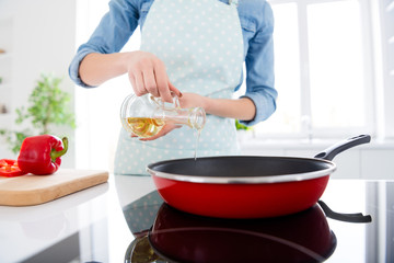 Cropped photo of beautiful housewife hold olive oil pouring hot frying pan enjoy hobby morning cooking tasty dinner family stand bright light kitchen indoors casual clothing