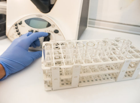 Hand with glove working in a laboratory with centrifuge and rack with test tubes