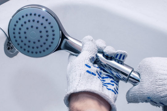 Repairman mounts a shower hose. Close-up of gloved hands. Cold blue tint