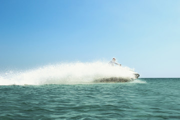 Obraz premium Vacation at sea in hot Sunny weather, A person on a jet ski rides on the sea water very fast with splashes around it against the blue sky, rest in the fresh sea air, travel by sea