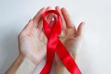 Red ribbon with a needle from a syringe, in the hand on a white background - this is an international symbol of the fight against AIDS