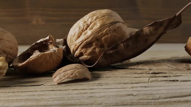 Tracking shot of still life with walnuts and leaves on a rough wooden board.