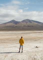 Tourist Man. Dry, barren landscape mountain background.  Dramatic desert, snowcapped mountains wilderness. Mountain range view. Salt Flats of Uyuni, Bolivia. Blue sky, nature, hiking, and sand dust