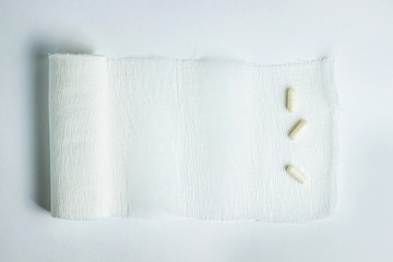 Medicine concept. Three tablets in capsules lie on a deployed bandage. The bandage lies on a white background. Photo from the top.