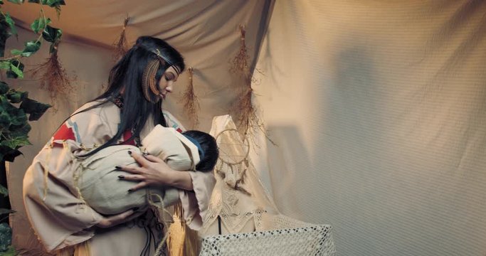 Beautiful young native american mother is rocking her child and looking, 4k