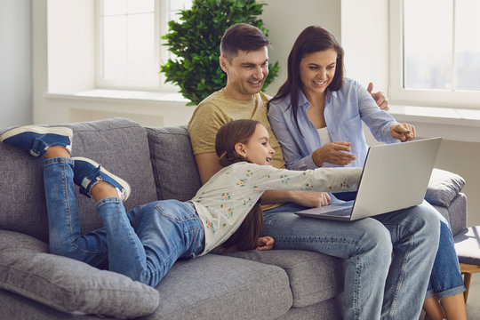 Family Laptop Online. Parents And A Kid Child Look At A Laptop At Their Leisure In A Weekend At Home.