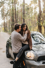 Naklejka premium beautiful young couple in love kisses and hugs sitting on a car