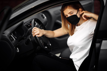 Fototapeta na wymiar Young woman driving car with protective mask on her face. Healthcare, virus protection, allergy protection concept.