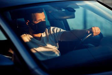 Portrait of man wearing disposable medical facemask in a car during coronavirus outbreak. Safety in the city.