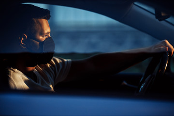 Portrait of man wearing disposable medical facemask in a car during coronavirus outbreak. Safety in the city.