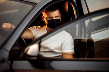 Attractive man driver in medical face mask inside the grey car, concept of coronavirus quarantine