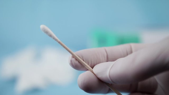 Close up of nurse with white gloves holding swab for coronavirus testing. Medical environment.